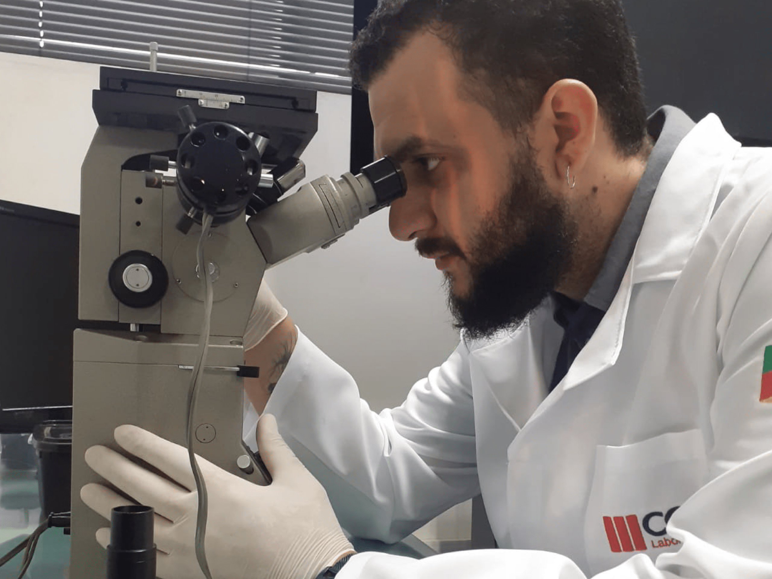 imagem ilustra um laboratorio acreditado, apresenta um técnico analisando um material em um microscópio